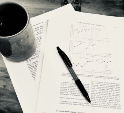 一杯咖啡、一支筆和行為科學期刊文章,其中包含圖表示實現目標的進展。